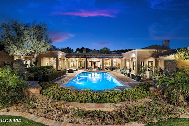 back of property at dusk with a patio, stucco siding, an outdoor pool, and a chimney