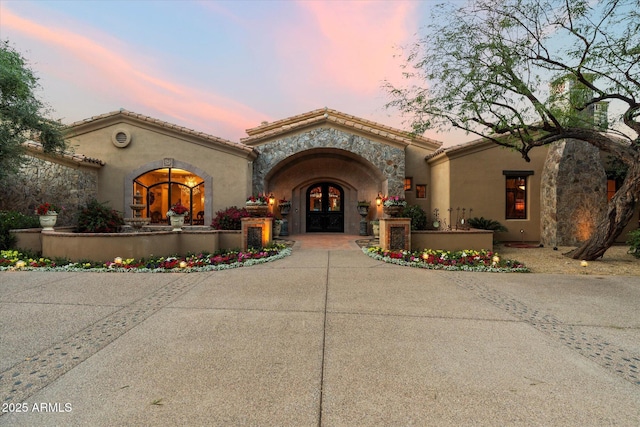 mediterranean / spanish-style house with a tiled roof, french doors, stone siding, and stucco siding