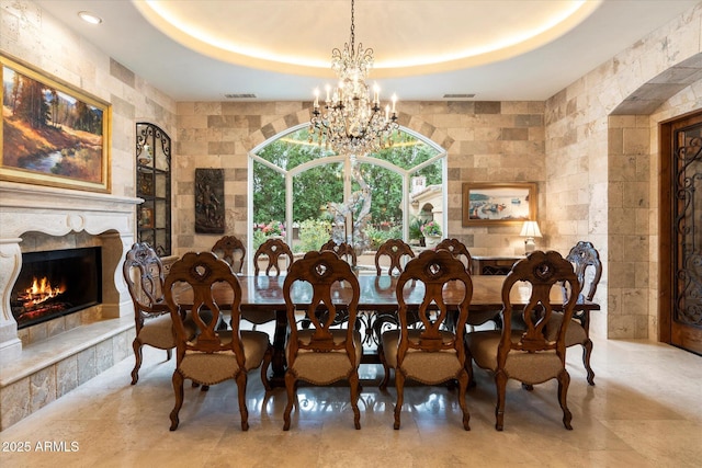 dining room with an inviting chandelier, visible vents, a raised ceiling, and a premium fireplace