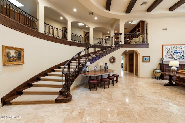 stairs featuring beam ceiling, visible vents, arched walkways, and a high ceiling