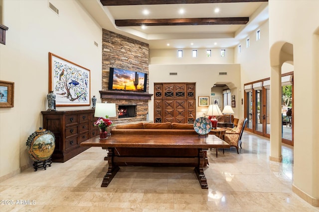 living room with visible vents, beamed ceiling, french doors, arched walkways, and a stone fireplace