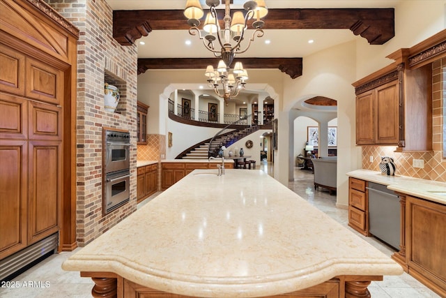 kitchen with arched walkways, stainless steel appliances, decorative backsplash, a notable chandelier, and brown cabinets