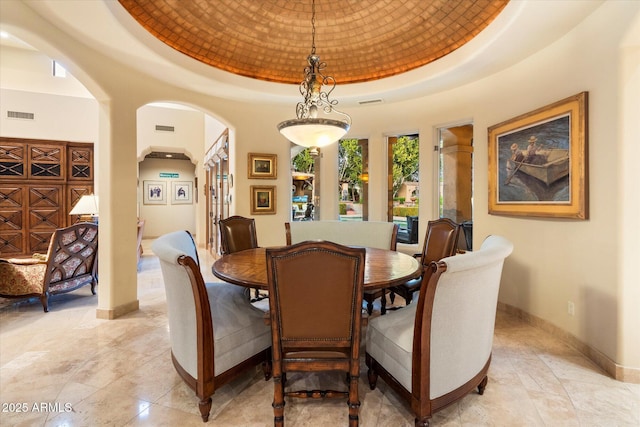 dining space featuring baseboards, a tray ceiling, arched walkways, and visible vents