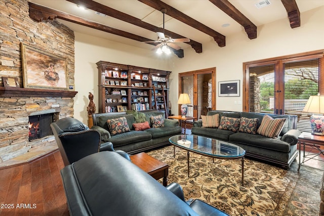 living room with visible vents, beamed ceiling, a stone fireplace, wood finished floors, and a ceiling fan