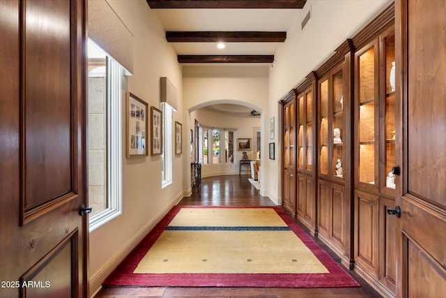 corridor featuring dark wood-style floors, baseboards, visible vents, beam ceiling, and arched walkways