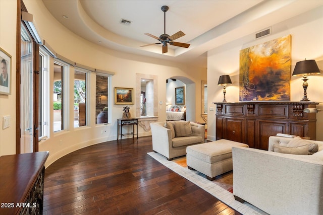 living room with visible vents, ceiling fan, a tray ceiling, arched walkways, and wood-type flooring