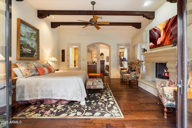 bedroom with beamed ceiling, arched walkways, a lit fireplace, and hardwood / wood-style flooring