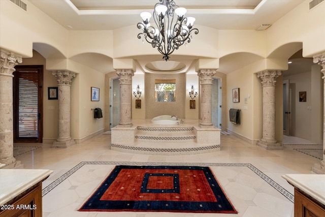 interior space with a tray ceiling, visible vents, baseboards, and ornate columns