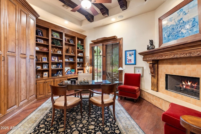 office featuring visible vents, beamed ceiling, a lit fireplace, wood finished floors, and a ceiling fan