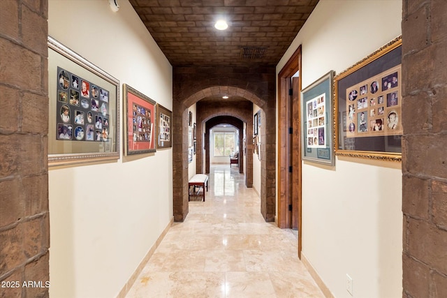 corridor featuring visible vents, brick ceiling, baseboards, and arched walkways