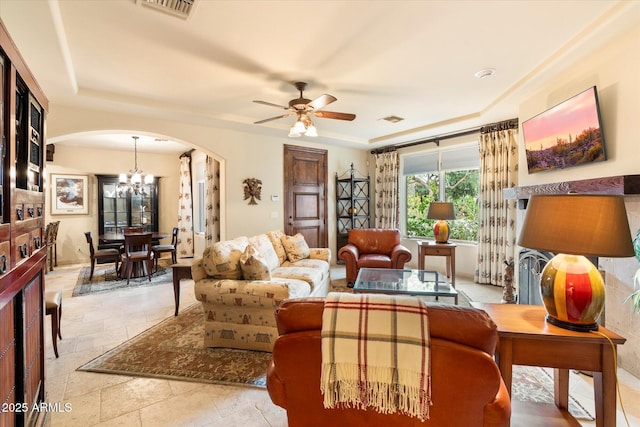 living room featuring visible vents, arched walkways, a raised ceiling, and ceiling fan with notable chandelier