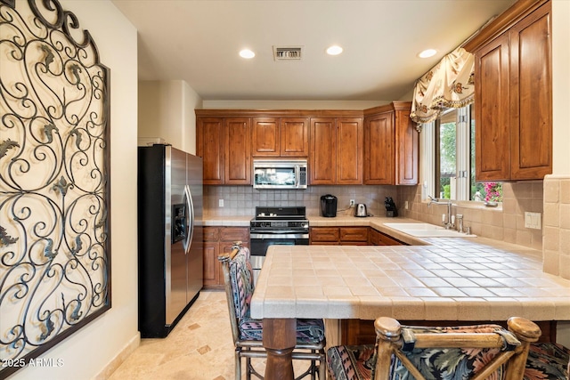 kitchen with visible vents, a peninsula, a sink, appliances with stainless steel finishes, and backsplash