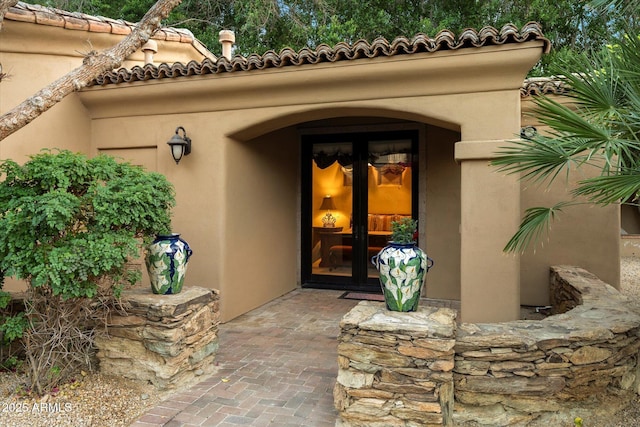 view of exterior entry with a tile roof and stucco siding