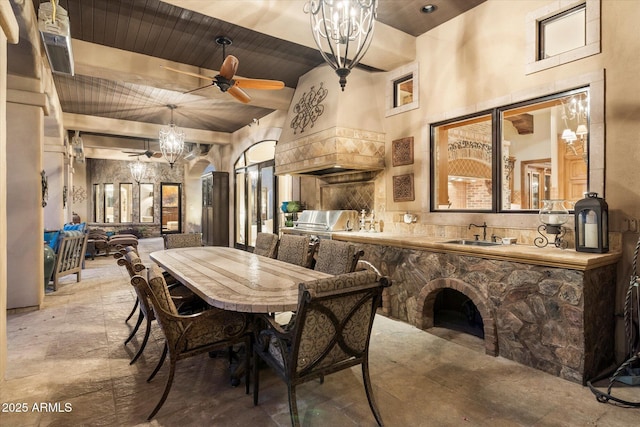 dining room featuring stone finish flooring, bar area, wood ceiling, ceiling fan with notable chandelier, and a towering ceiling