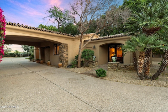 view of front of property with a tiled roof, stone siding, driveway, and stucco siding