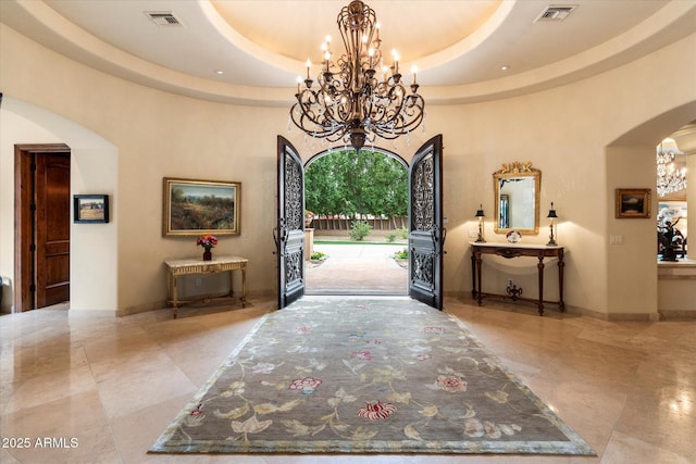 foyer entrance featuring visible vents, baseboards, arched walkways, a raised ceiling, and a chandelier