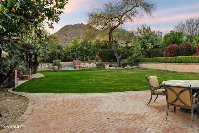 patio terrace at dusk featuring a mountain view and a yard