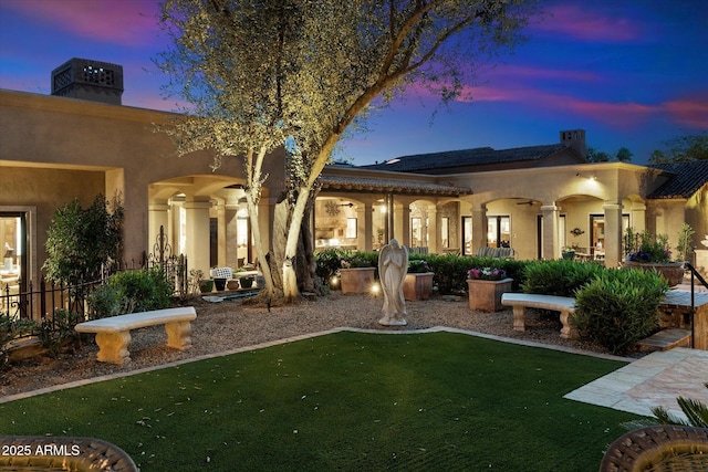 rear view of property with stucco siding, a lawn, and a chimney