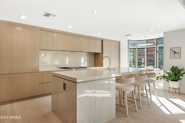 kitchen featuring light countertops, visible vents, a sink, an island with sink, and a kitchen breakfast bar