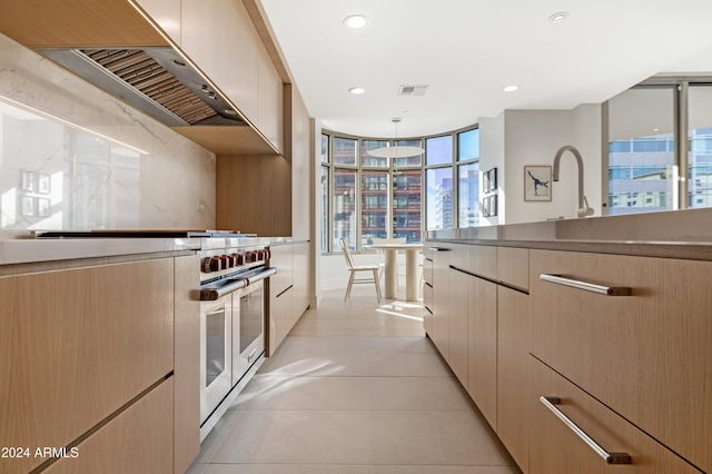 kitchen featuring wall chimney range hood, dark countertops, light brown cabinets, and visible vents