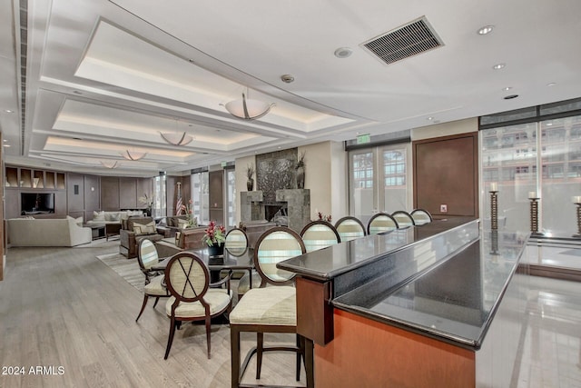 kitchen with light wood finished floors, visible vents, open floor plan, a tray ceiling, and a fireplace