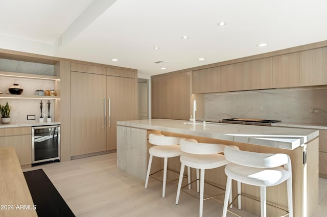 kitchen featuring light countertops, an island with sink, modern cabinets, beverage cooler, and a kitchen breakfast bar