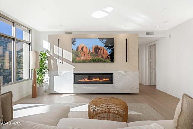 living area with light wood finished floors, a glass covered fireplace, visible vents, and baseboards