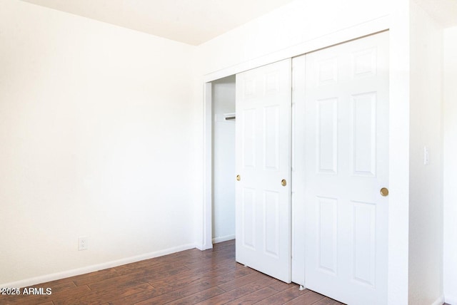 unfurnished bedroom with baseboards, a closet, and dark wood-style floors