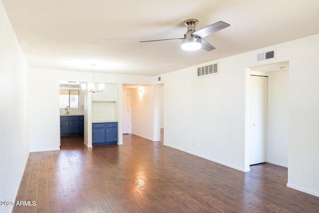 unfurnished living room with a sink, ceiling fan with notable chandelier, dark wood-style floors, and visible vents