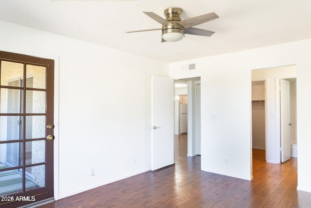 unfurnished bedroom with freestanding refrigerator, dark wood finished floors, visible vents, and baseboards