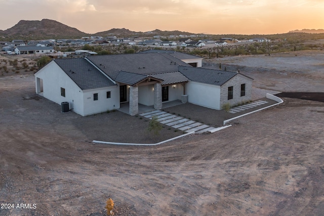 view of front of home with a mountain view, stone siding, central AC unit, and stucco siding