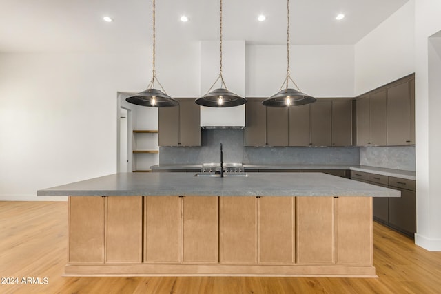 kitchen with tasteful backsplash, light wood-style flooring, a high ceiling, stainless steel gas stovetop, and a large island