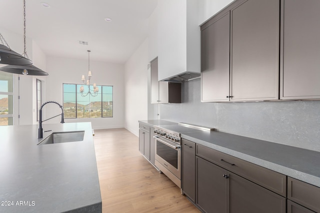 kitchen featuring backsplash, light wood-type flooring, custom exhaust hood, stainless steel range, and a sink