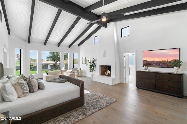 bedroom with high vaulted ceiling, wood-type flooring, a large fireplace, and beamed ceiling