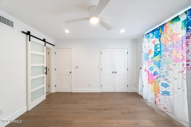 unfurnished bedroom featuring a barn door, a closet, ceiling fan, and hardwood / wood-style floors