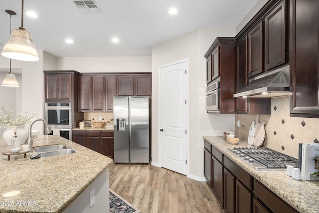 kitchen featuring light stone countertops, light hardwood / wood-style flooring, decorative light fixtures, appliances with stainless steel finishes, and sink