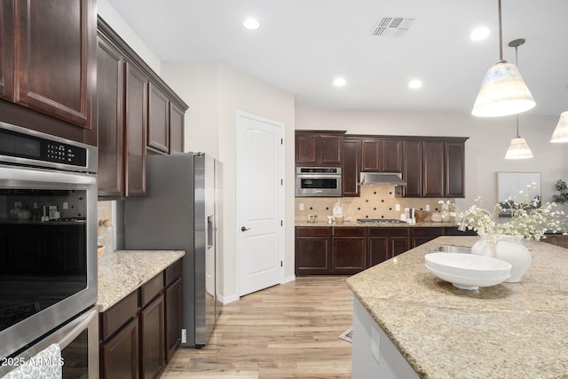 kitchen featuring stainless steel appliances, light wood-type flooring, light stone countertops, decorative backsplash, and decorative light fixtures