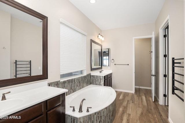 bathroom with a relaxing tiled tub, vanity, and wood-type flooring