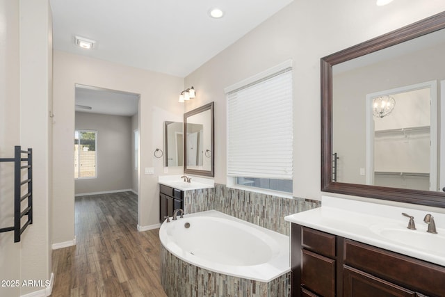 bathroom with tiled bath, an inviting chandelier, wood-type flooring, and vanity