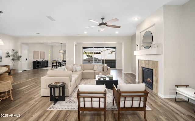 living room featuring a tiled fireplace, ceiling fan, and wood-type flooring