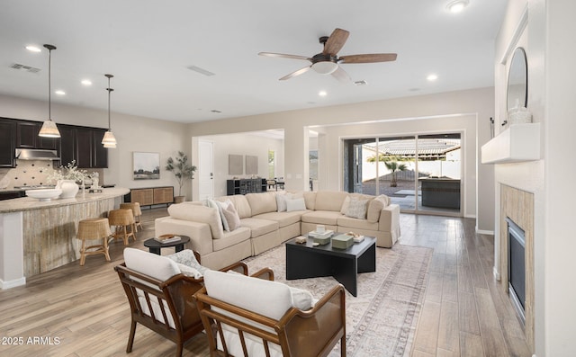 living room with a tile fireplace, ceiling fan, and light hardwood / wood-style flooring