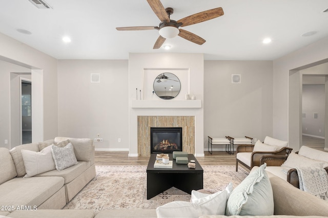 living room featuring a tiled fireplace, ceiling fan, and light wood-type flooring