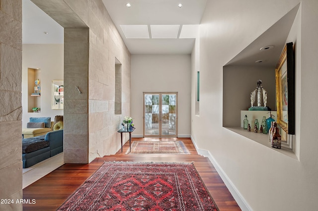 corridor with wood finished floors, a towering ceiling, and baseboards