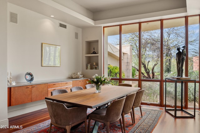 dining area featuring built in shelves, a healthy amount of sunlight, visible vents, and wood finished floors