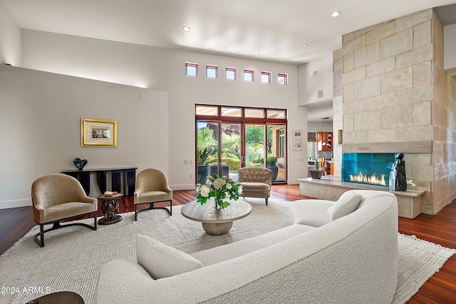 living room with a fireplace, a towering ceiling, baseboards, and wood finished floors