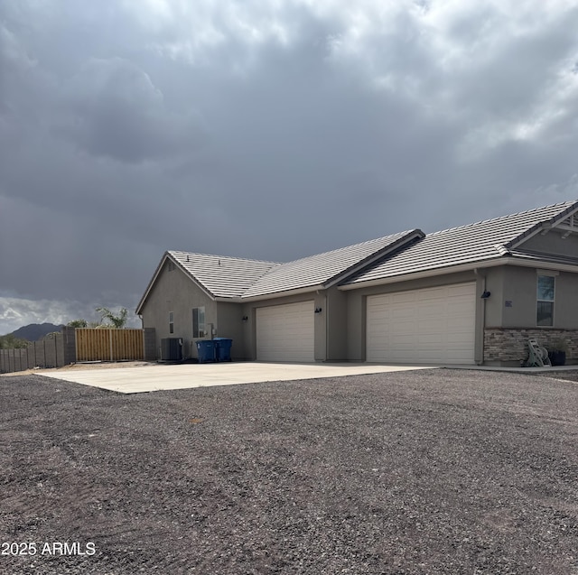 view of front of property featuring central AC, fence, a garage, stone siding, and driveway