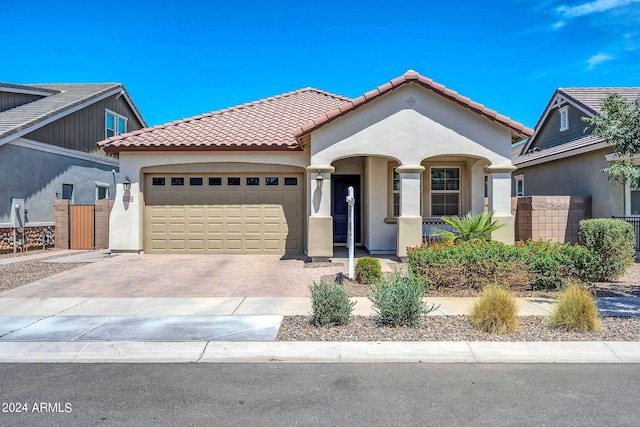 mediterranean / spanish home with a tile roof, an attached garage, fence, decorative driveway, and stucco siding