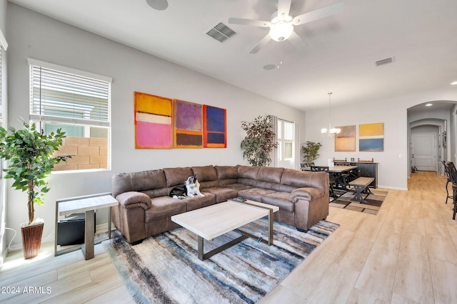 living area with arched walkways, visible vents, light wood finished floors, and ceiling fan with notable chandelier