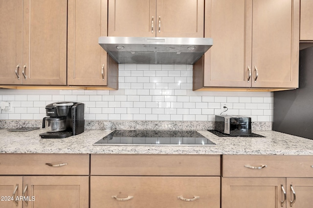 kitchen featuring light stone counters, backsplash, black electric cooktop, and under cabinet range hood