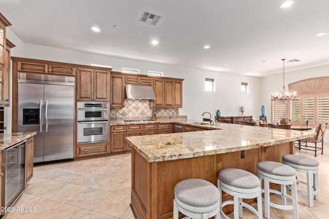 8689 E Krail St, Scottsdale, AZ 85250 - kitchen featuring appliances with stainless steel finishes, beverage cooler, under cabinet range hood, brown cabinetry, and recessed lighting
